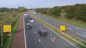 Busy motorway with lane closure and slowed traffic with trains traveling in both directions on left of frame. Time lapse 15x. M6 motorway, North Lancashire, England, UK.