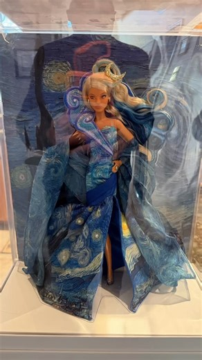 This Barbie doll embodies the timeless beauty, wonder, and enchantment of Vincent van Gogh’s The Starry Night, which is on display at The Museum of Modern Art (MoMA) in New York City. Inspired by the artwork, her windswept curls frame a yellow crescent moon, and her gown incorporates other symbolic elements, from the whirls of wind on her bodice to the tranquil village resting along the hemline. Her single black glove continues the impression of the cypress tree from her dress, and her sculpted