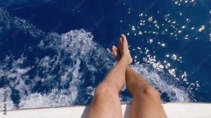 Top view of men's bare feet dangling from the side of the ship. First person view. Men's feet against a background of sparkling, frothy white sea waves. Walking on the sea. Slow motion