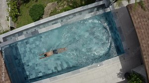 Aerial view of a modern residential swimming pool, a man jumps into the pool with clear water in a luxurious setting