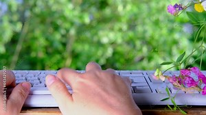 female hand tipping text on laptop keyboard in the garden against the background of green trees in summer, concept of the daily routine of a freelancer, programmer, downshifter