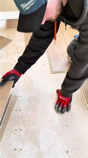 Worker installing click-lock laminate wood flooring over a subfloor using red and black gloves