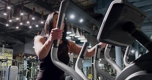 Beautiful woman on cardio area in gym 4k video. Fitness girl training on elliptical exercise machine. Athletes weight loss workout.