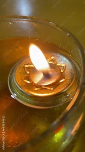 A floating candle casts its warm, flickering glow inside a glass filled with oil, creating an enchanting and serene ambiance