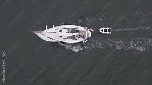 topdown above top down aerial drone 4K film of sailboat yacht sail sailing on sea ocean water with Dutch holland flag and attached towed dinghy rubber boat