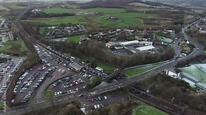 Low level aerial footage approaching Croy railway station on the Glasgow to Edinburgh line as a passenger train arrives.