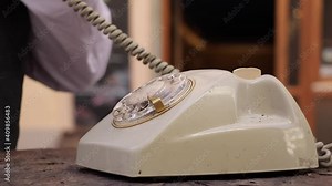 Close-up view of a hand picking up the telephone receiver and dialing two numbers on an old rotary phone.