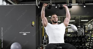 Active bodybuilder, young man lifting heavy weights black dumbbells concentrating working out alone. Gym concept. Healthy lifestyle.
