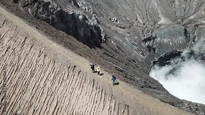 4K Tracking Couple walking by drone on adventure walkway at top of active Volcano with smoke at Mount Bromo (Pananjakan Peak) in Java island, Indonesia. Abstract for freedom life and creative.