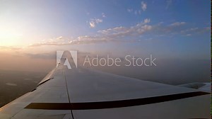4K, Beautiful twilight and clouds from above. Wing of the plane and the orange sunset as seen through an airplane window during the flight. Passenger POV traveling by air.-Dan