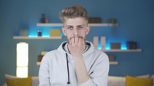 Young man biting his nails is worried and needs to think in a panic. Young man biting his nails looking worried and panicked in front of the camera at home.