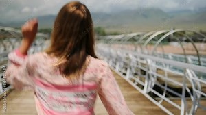 Rear view woman dancing in long dress on wooden pier overlooking the ocean enjoying her vacation on summer trip.
