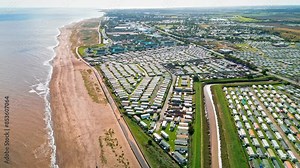 Aerial video footage of the seaside town of Ingoldmells in Lincolnshire, showing the beach, funfair, holiday homes, caravans, and sea.