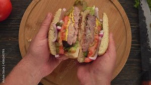 Top view of the male hands opening fresh homemade grilled burger with meat cutlet cut in two halves. Fresh homemade grilled burger with meat cutlet, tomatoes, lettuce, onion.