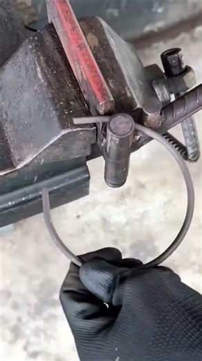 bending a long metal rod into a circular shape using a manual steel bending tool in the workshop