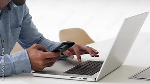 Man sit at desk, multitasking with smartphone in one hand while typing on laptop, close up. Engagement in remote tasks, research, communication, data entry, integration of technology in daily workflow