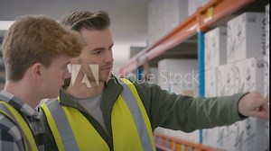 Male team leader in distribution warehouse explaining to intern how to use digital tablet to manage stock control - shot in slow motion