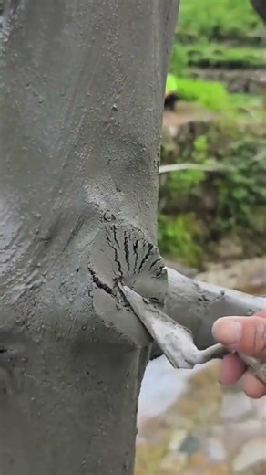 applying mortar to a concrete tree with a small metal tool to create a realistic bark texture finish