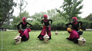 Three african women are dancing a folk traditional dance on a grass meadow, in traditional costumes with wicker baskets, sunny, trees' background, African costumes, traditions, African culture, tribes