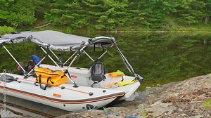 Lonely moored fishing trolling boat floating and drifting at lake bank at wilderness lake. Anchored to small island empty boat. Inflatable motorized boat with tent swaying on tranquil water at morning