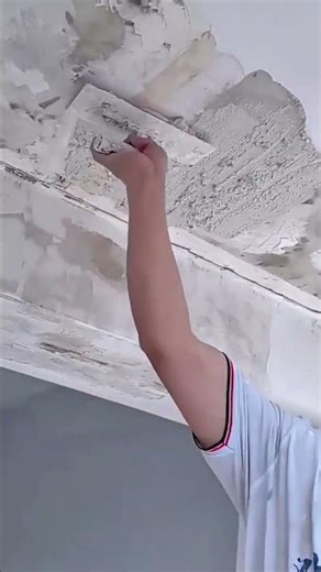 A person is applying white spackling compound to a rough textured ceiling beam