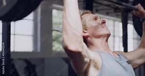 Young male bodybuilder training with a barbell in a gym. Determined muscular man using weights during his heavy weightlifting exercise. A sporty powerlifter pumping iron and building strong muscles