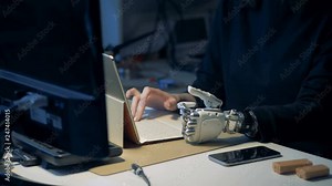 Disabled person with bionic hand types on a laptop. Metal prosthetic hand working.