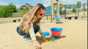 Little girl child playing sand on the playground. Kid playing in the sand on the playground. Healthy active baby outdoors plays games concept.