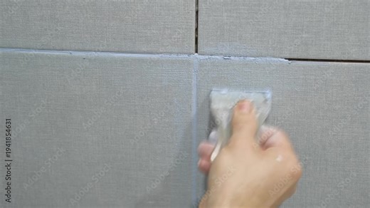 Worker using a rubber grout float to smooth grout between tiles. Carefully applying sealant to tiles joints. Workman hands smoothing caulk, using small tool to remove excess and create clean seam.