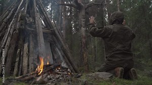 a man in the forest worships the idol of the ancient forest gods next to a fire and a small pagan temple