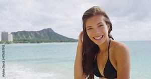 Happy young woman walking on shore at Waikiki Beach. Cheerful female tourist is playing with hair during wearing bikini on vacation at in Honolulu, Oahu, Hawaii.