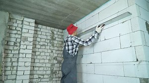builder checking markings on aerated concrete block wall with construction ruler