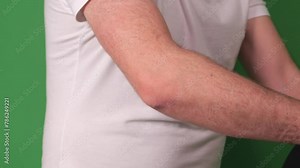 Man shows off an elbow brace's functionality by flexing his arm, explaining its use in rehabilitation post-injury on a green backdrop.