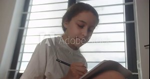 Cute preteen school girl pupil studying at home. Teenage girl expressing lonely thoughts while sitting on bed in her room. Smiling smart little girl writes in a notepad. 4K