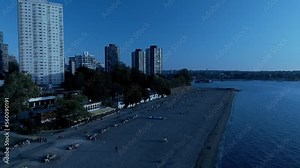 English Bay Sunset Beach reveal pan drone overlooking commercial properties of Davie and Denman pubs restaurants condominiums apartments hotels shops sunny summer day skyline lush greenery post modern