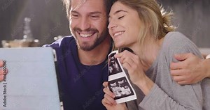 A married couple in love videocall their parents using a tablet, to announce the birth of their son showing the ultrasound. Concept of: family, birth, life, love
