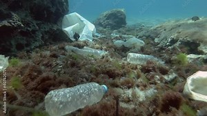 Slow motion. Plastic pollution of the ocean bottom, Tropical fishes swims over the bottom covered with a lot of plastic garbage. Bottles, bags and other plastic debris on seabed in Mediterranean Sea