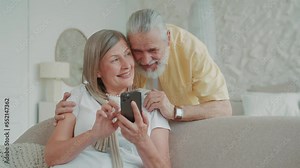 Elderly couple use smartphone relaxing together on sofa at home smiling feel happy. Have fun enjoy mobile application and watch video on internet. Modern gadget. Communication. Close up