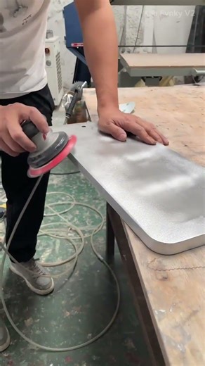 A person sanding a flat surface using a power sander tool.
