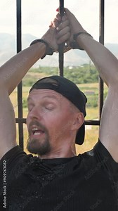 Vertical: A captive man handcuffed to a cage has cold water splashed in his face. Illegal cruel treatment of prisoners in prison. Torture of prisoners. Methods of physical violence in prison