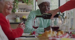 Animation of christmas greetings text over diverse friends at christmas meal table. Christmas tradition, celebration and festivity concept digitally generated video.