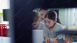 Medium shot of three classmates, two girls and one boy, talking to each other while using laptop computer at desk during information technology lesson