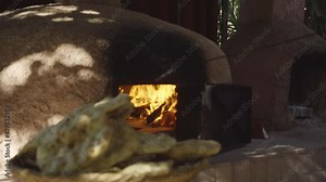 Slow motion shot of woman cooking bread in a traditional wood fired clay oven