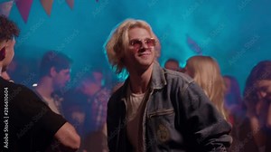 Attractive blonde guy dancing at the party setting the rhythm cheering up his friends hanging out together in an city life night club.