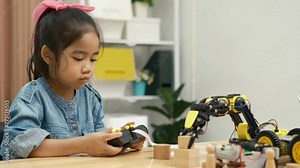 A primary school girl focuses on operating a robotic arm with a remote control, demonstrating STEM education in action. Stock Video