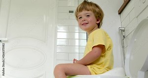Cute toddler boy sitting on toilet in bathroom at home