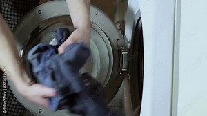 Men's hands load the laundry into the washing machine. Preparing the laundry for washing. The washing machine is viewed from the side. Close-up.