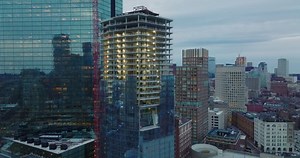 Pull back shot of tall building construction site. Revealing tower crane and high rise modern skyscraper with glossy facade. Boston, USA
