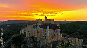 Cinematic panoramic view of feudal square-shaped castle on a riverside clifftop at golden sunset in France. Aerial view of Château de Beynac fortress at golden hour in France.