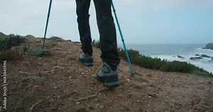 Close up reveal shot, camera follow man walk on path or trail. Lens move from bottom to top, show hiking shoes, jacket, backpack and trekking poles. Young hispanic man in wilderness